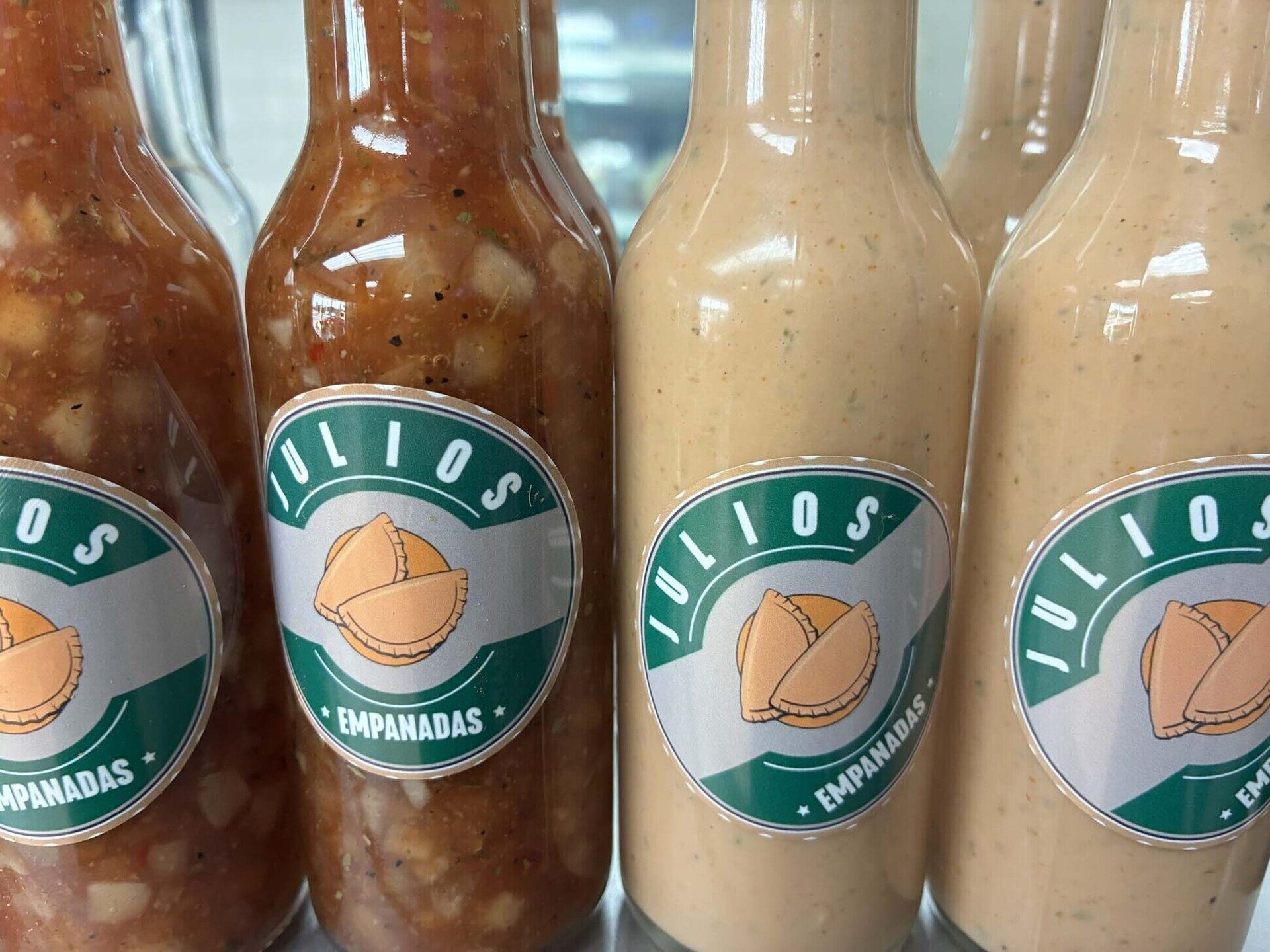 Four branded Julio's Empanadas sauce bottles with green and gold labels
